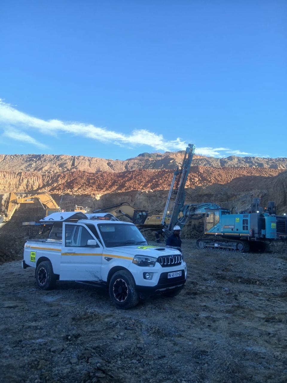 Opti-Blast site bakkie and drill rig against a highwall at sunrise