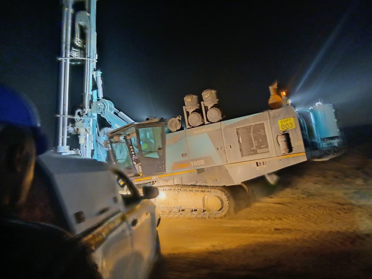 Two rigs and an excavator working an open pit blast area